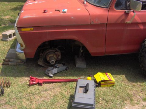 1979 Ford Bronco - Front wheel removed from a 1979 Ford Bronco during maintenance, with tools laid out on the grass.