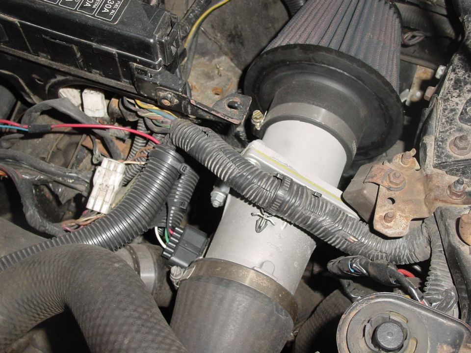 Engine intake tube with a black cone air filter and various wires and hoses connected
