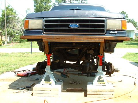 1995 Ford Bronco - Front end of a Ford truck is raised on jack stands for maintenance, revealing the chassis and suspension components.