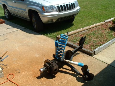 1995 Ford Bronco - A disassembled front suspension system lies on a driveway next to a silver Jeep Grand Cherokee.