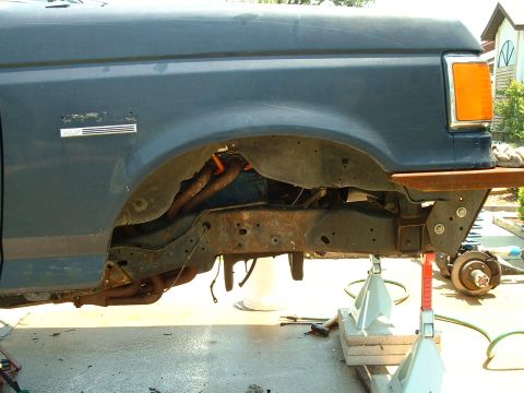 1995 Ford Bronco - The side of a 1995 Ford Bronco is visible, with the fender and frame exposed as the vehicle is supported by jack stands.