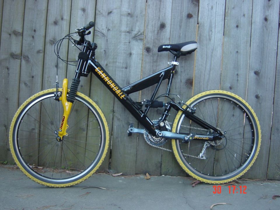 Black Cannondale mountain bike with yellow fork and tires leaning against a wooden fence