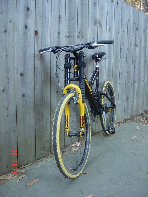 1990 Ford Bronco - A black mountain bike with yellow accents is parked against a weathered wooden fence.