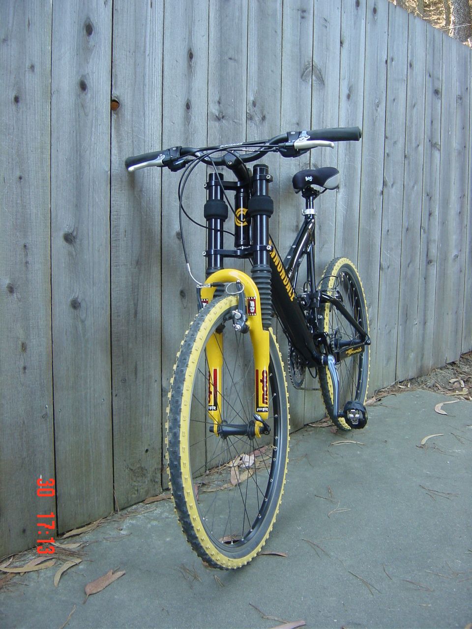 Black mountain bike with yellow front forks and tires leaning against a wooden fence