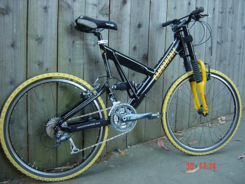 1990 Ford Bronco - This black full suspension bicycle features yellow tires and a yellow front fork, leaning against a wooden fence.