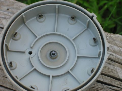 1995 Ford Bronco - Back side of a gray plastic wheel center cap resting on weathered wood, showing its molded reinforcing ribs, center hub, and retention tabs…