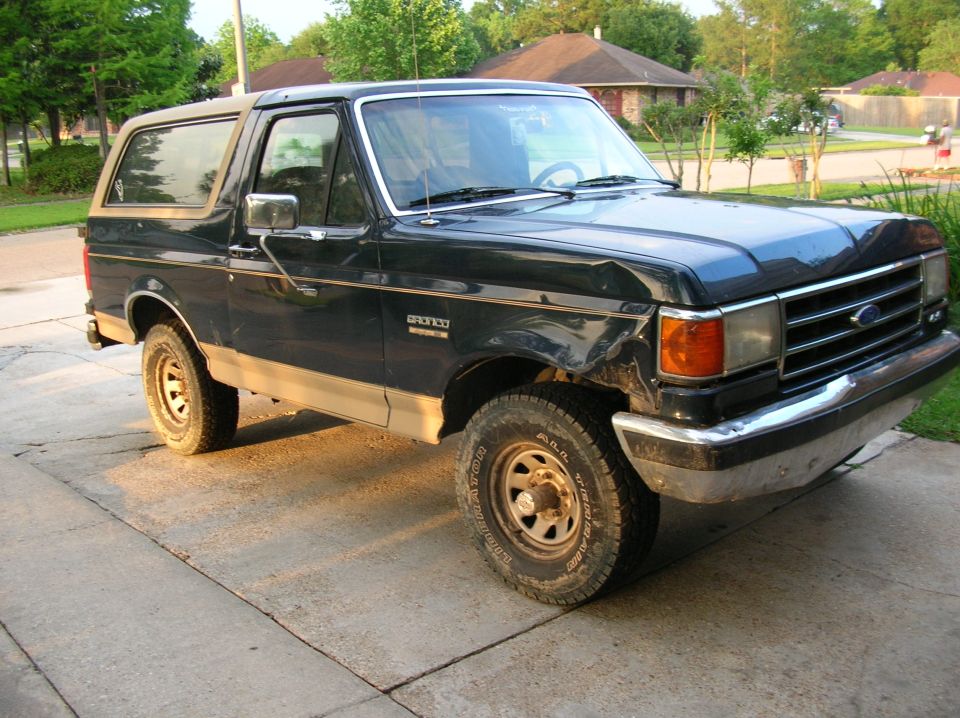 Dark green two-tone Ford Bronco SUV with chrome grille parked on a concrete driveway, seen from front passenger side