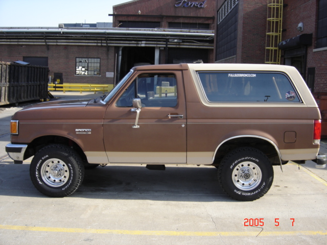 Brown and tan Ford Bronco parked side-on in front of a brick industrial building