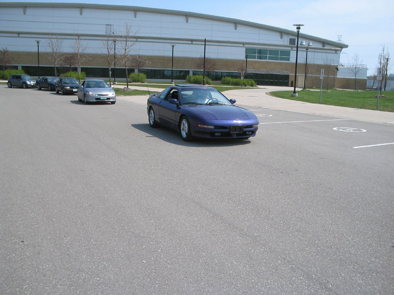 Purple Ford Probe coupe driving through a parking lot in front of a large white building