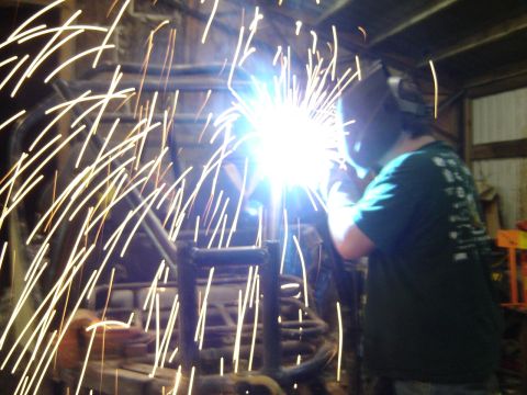 1989 Ford Bronco - A person welds metal in a dimly lit garage, surrounded by a shower of sparks.