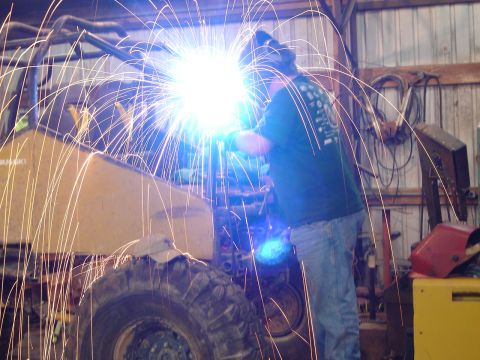1989 Ford Bronco - A person welds on a vehicle frame, creating a shower of sparks. The scene takes place inside a workshop.