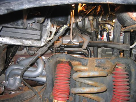 1995 Ford Bronco - Underhood view looking down past the front suspension, showing a coil spring with red-booted shock absorbers, rusty radius arm bracket and…