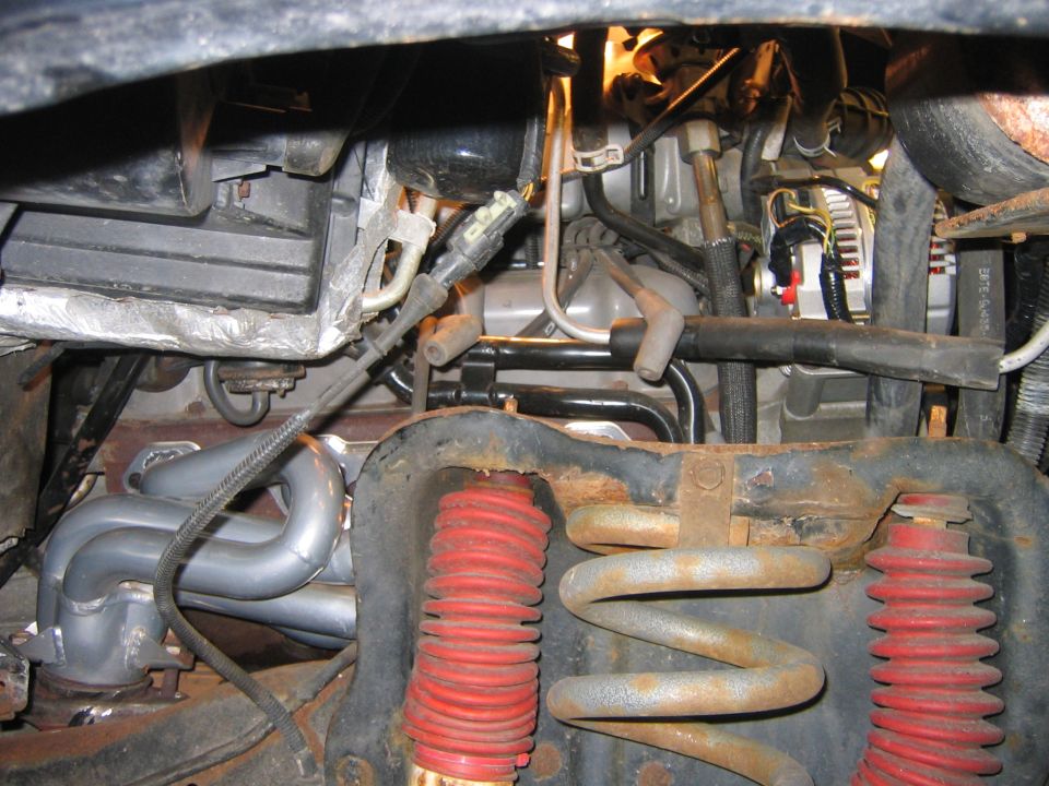 Front coil spring, red-booted shocks and silver tube header seen under a truck's hood