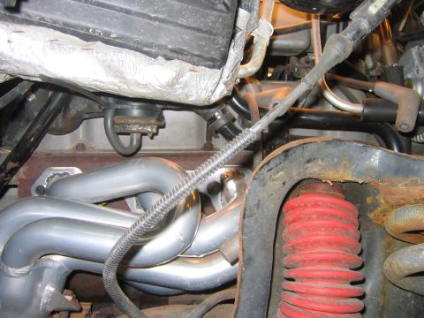 1995 Ford Bronco - Tight underhood shot of a silver-coated tubular exhaust header bolted to the cylinder head, with a loomed cable and spark plug wires routed…