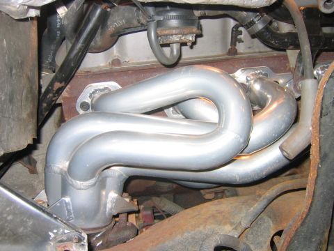 1995 Ford Bronco - Close-up under the hood of a newly installed silver-coated tubular exhaust header, its four welded primary tubes curving down into a collec…