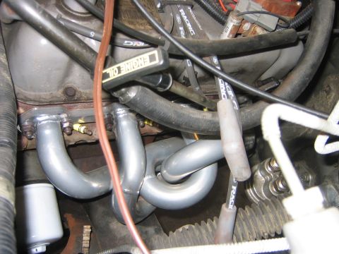 1995 Ford Bronco - Tight engine-bay view of gray-coated tubular exhaust headers wrapping around spark plugs on a V8, with black Ford Racing plug wires routed…