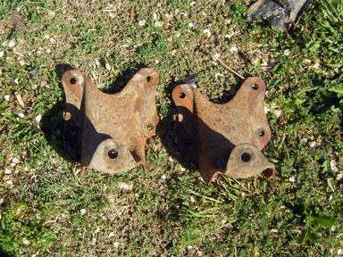 1995 Ford Bronco - Two old, rusty metal brackets lie on the ground covered in grass and dirt.