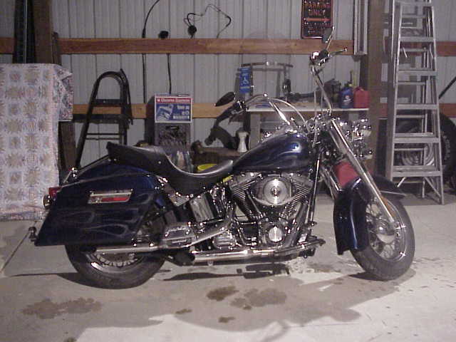 Blue ghost-flame cruiser motorcycle with saddlebags parked in a metal shop