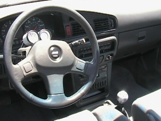 Gray coupe interior with column-mounted aftermarket gauges and white shift knob