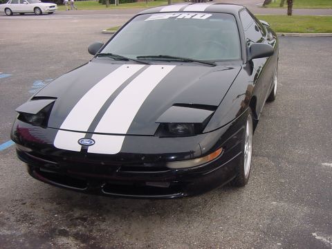 1997 Ford Probe - A black Ford Probe with racing stripes is parked in a lot. The car has pop-up headlights and a Ford emblem on the grille.