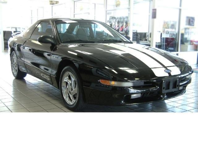 Black coupe with white racing stripes and chrome wheels, front 3/4 view indoors