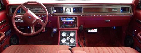 1985 Ford LTD Crown Victoria - Wide interior shot across the red dashboard and red cloth bench seat of a Ford LTD Crown Victoria, showing the horizontal sweep speedometer…