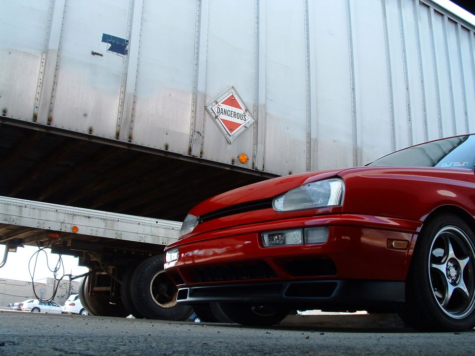 Red 1994 Volkswagen Jetta front 3/4 view next to a semi-trailer with a 'Dangerous' placard