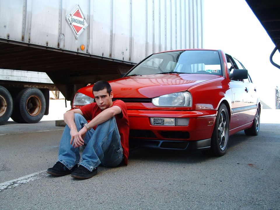 Red Volkswagen Golf Mk3 parked next to a trailer with a guy sitting in front
