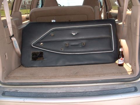 1978 Ford Mustang II - A black door panel a chrome trim accent and a horse emblem, consistent with a 1978 Ford Mustang II, is stored in the cargo area of another…