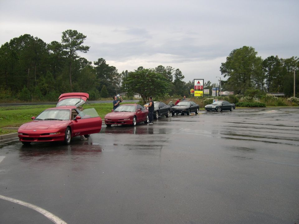 Row of coupes on a wet parking lot, red car in front with hood, hatch and door open