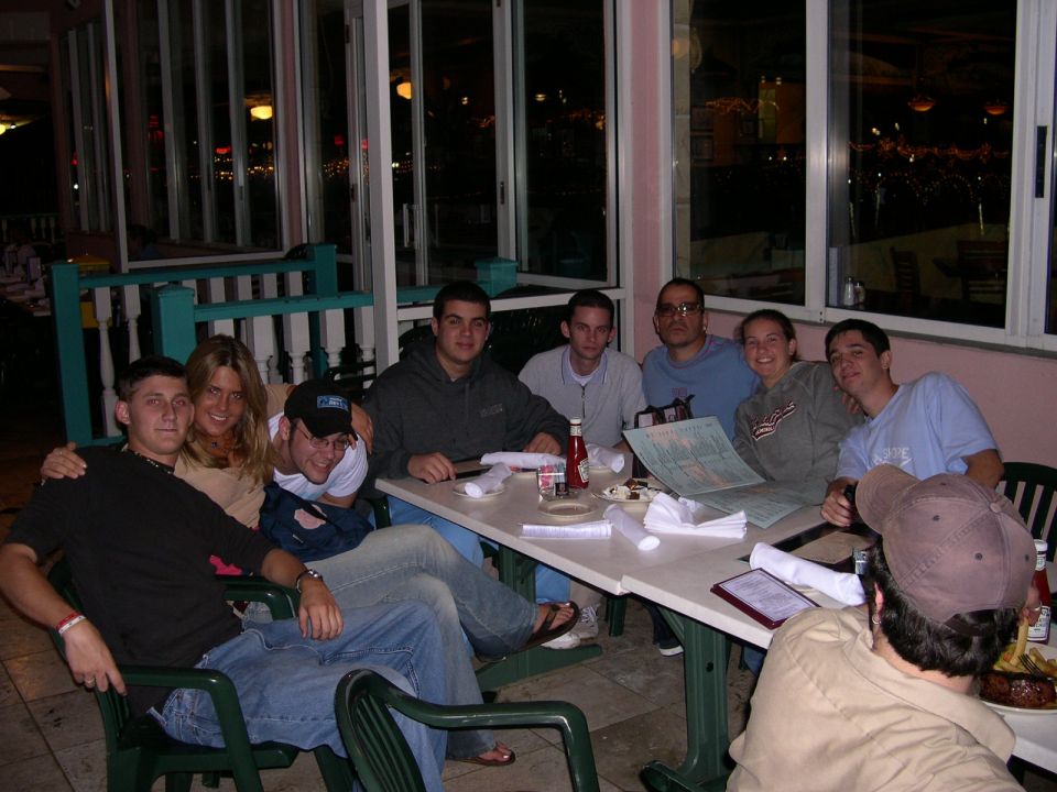Group of friends seated around restaurant tables with green chairs at night; no vehicle shown