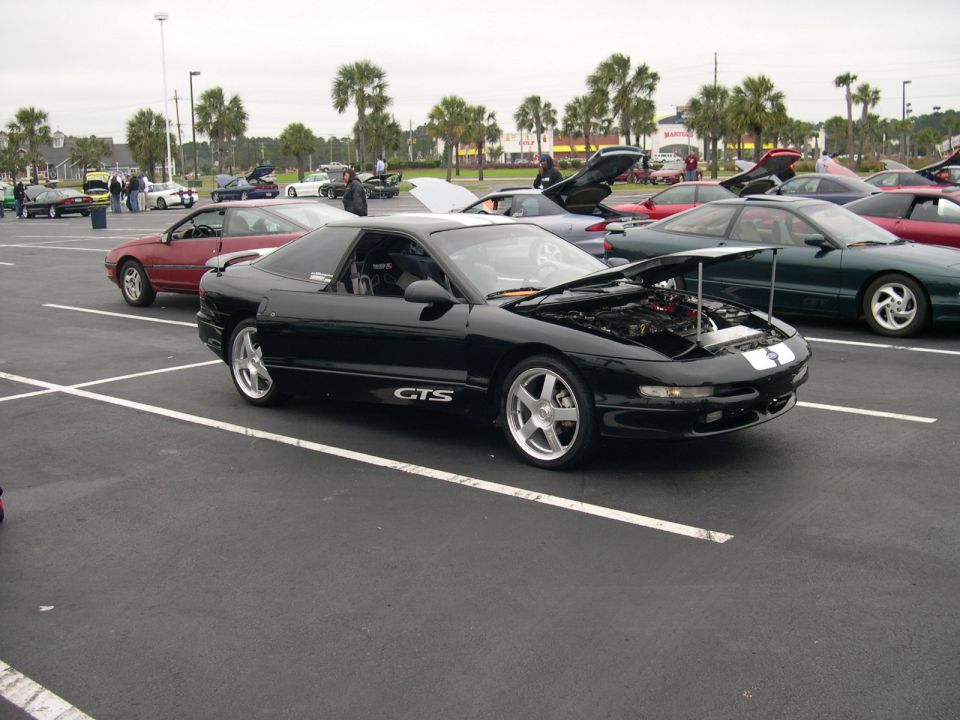 Black Ford Probe coupe with GTS door decal and open hood at an outdoor car show, 3/4 front view