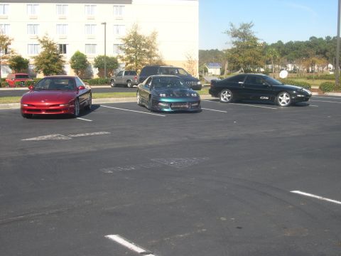 1997 Ford Probe - Three sports cars are parked in a lot outside a building.
