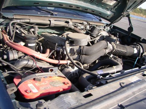 1995 Ford Bronco - The engine bay of a green 1995 Ford Bronco is visible, a red battery and various hoses.