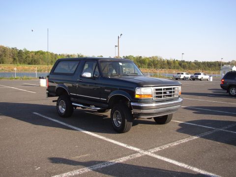 1995 Ford Bronco - Dark green two-door Ford Bronco full-size SUV with removable hardtop, shot from the front-right three-quarter angle in an empty striped par…