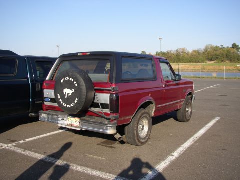 1995 Ford Bronco - Rear view of a red 1995 Ford Bronco with a spare tire on the back, parked in a lot.