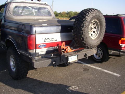 1995 Ford Bronco - Rear three-quarter view of a lifted dark blue Ford Bronco in a paved lot, fitted with a heavy steel rear bumper, D-ring shackle mounts, an…