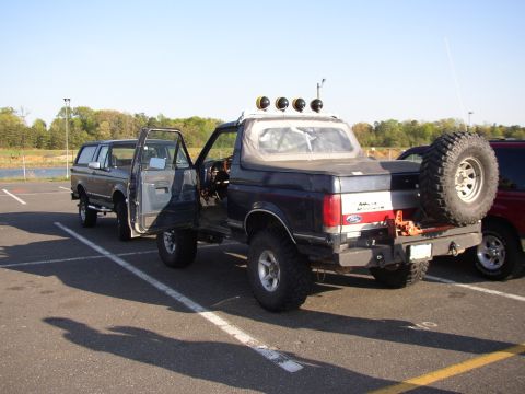 1995 Ford Bronco - Two Ford Broncos are parked in a lot, one with its doors open and a spare tire on the back.