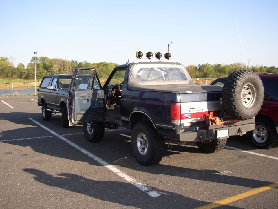 Dark blue Ford Bronco with a spare tire mounted on the rear, doors open, parked in a lot