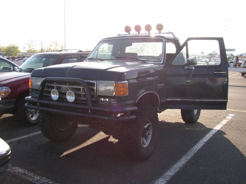 1995 Ford Bronco - Dark blue Ford pickup truck with off-road lights and bull bar parked in a lot.