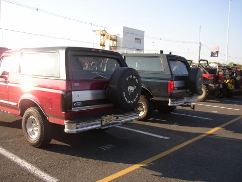 1995 Ford Bronco - Two Ford Broncos are parked in a lot, with a red one in the foreground and a dark green one behind it.