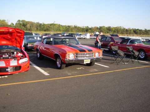 1995 Ford Bronco - A classic orange Chevrolet Chevelle SS is displayed at a car show, with other vehicles visible in the background.