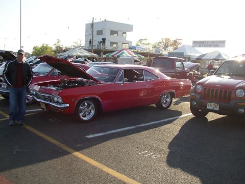 1995 Ford Bronco - A red 1965 coupe is displayed with its hood open at a car show, alongside other vehicles.