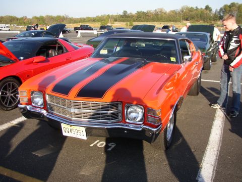 1995 Ford Bronco - A classic orange 1970 Chevrolet Chevelle SS is displayed at a car meet, with other vehicles in the background.
