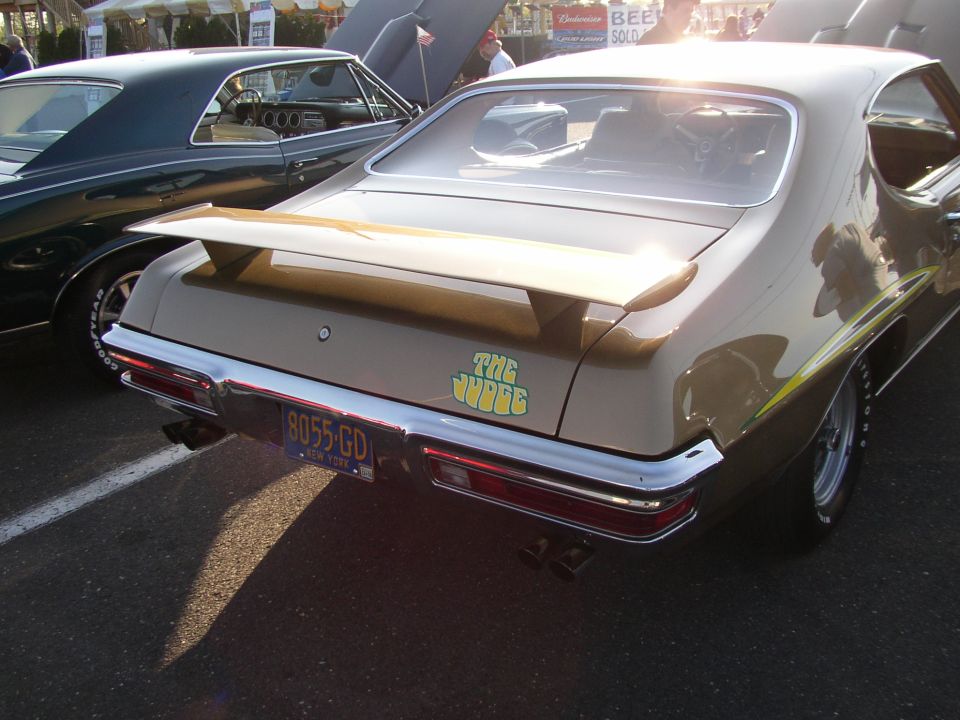 Rear of a gold Pontiac GTO with a spoiler and "The Judge" decal. Another car is parked next to it