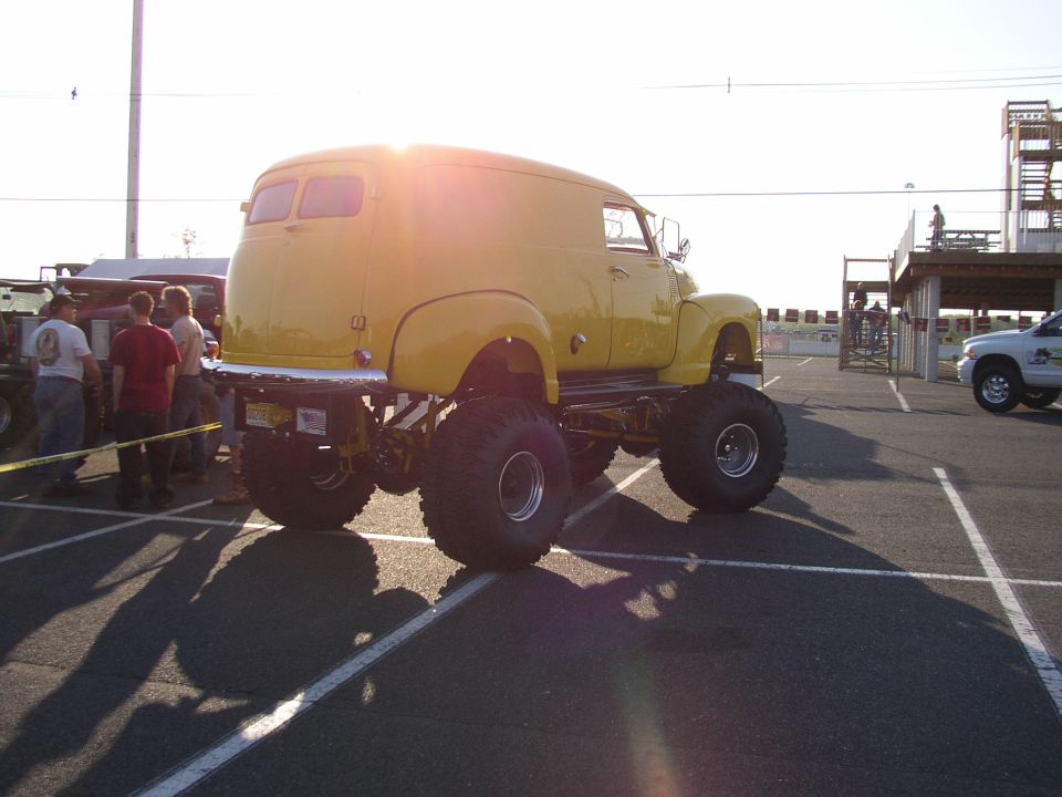 Yellow panel van monster truck with large tires, seen from a 3/4 front angle