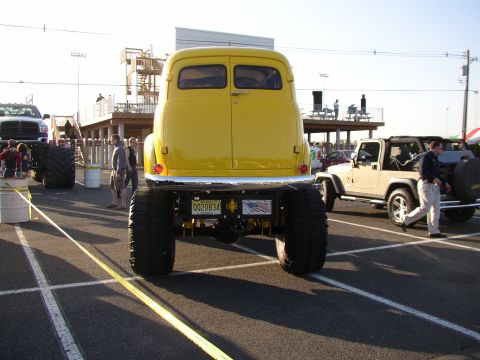 1995 Ford Bronco - Rear view of a yellow vintage panel truck built as a lifted 4x4 show rig, sitting on oversized mud tires with an exposed yellow-painted fra…