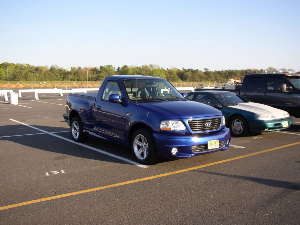 Blue Ford F-150 Lightning pickup truck parked in a lot. Other cars are visible behind it