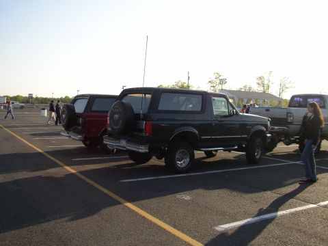 1995 Ford Bronco - Two Ford Broncos are parked side-by-side in a parking lot under a clear sky.