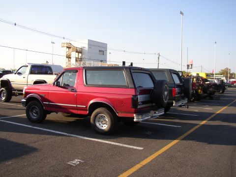 1995 Ford Bronco - A red 1995 Ford Bronco is parked in a lot alongside other vehicles on a sunny day.